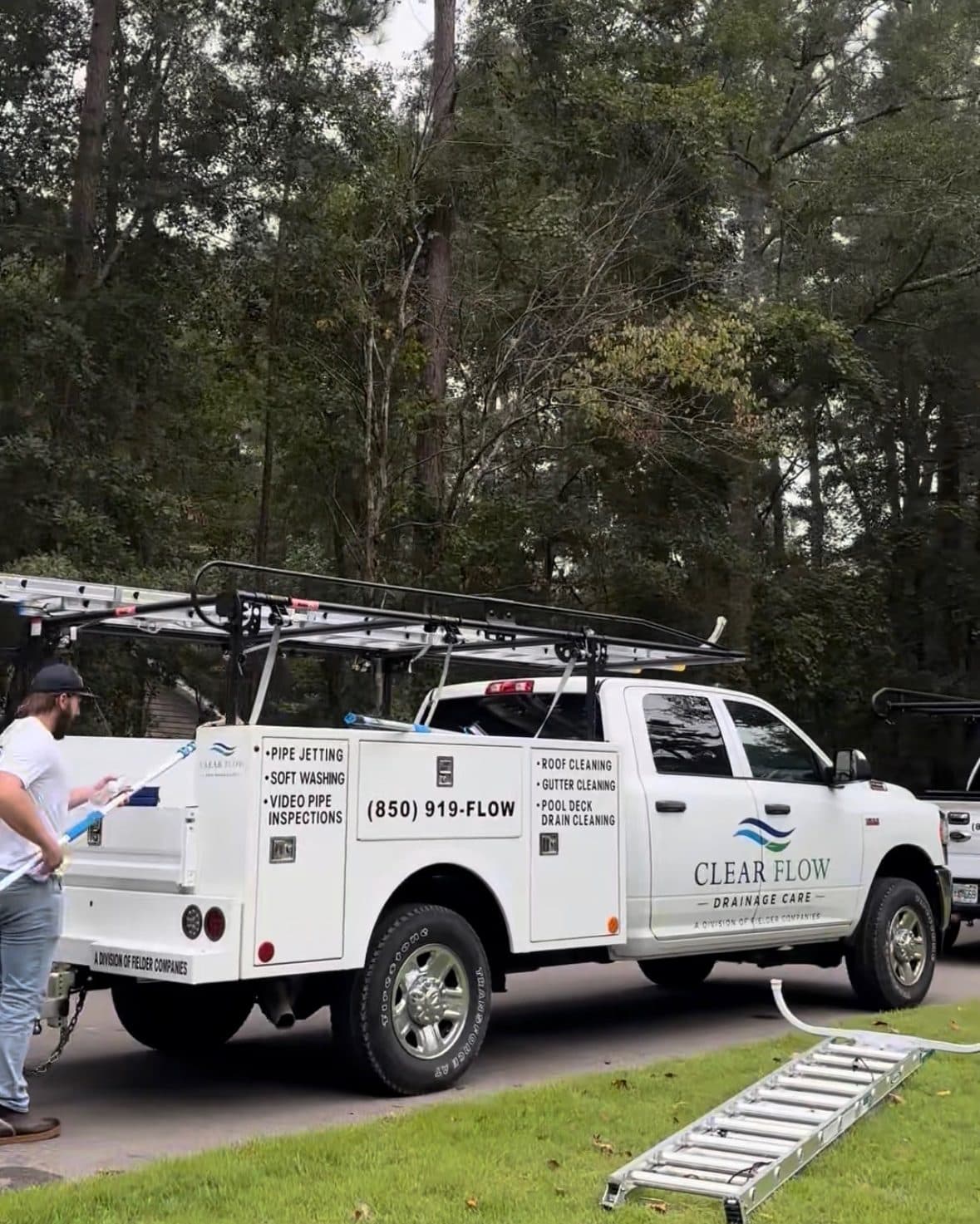 The Clear Flow pickup with its ladder rack and the jetting trailer parked at a Leon County job, a technician unloading beside it