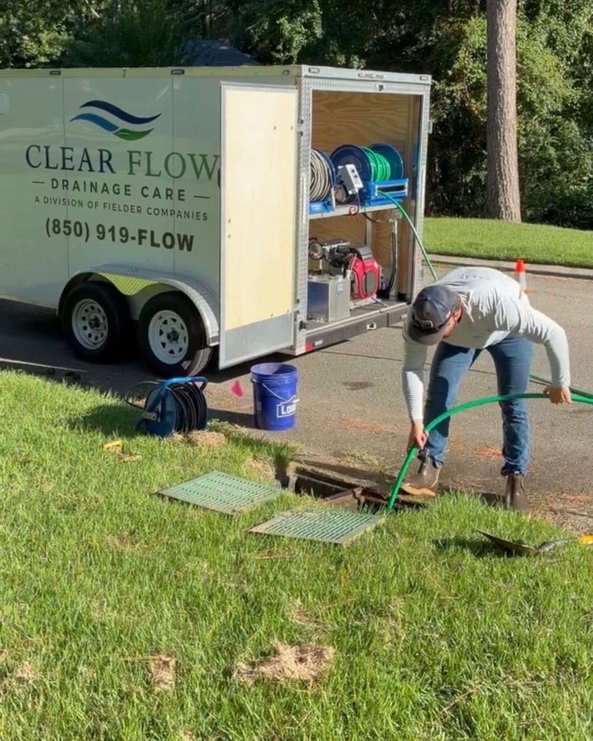 Clear Flow technician running a hose into a yard drain inlet to test how it takes water, with the jetting trailer behind him on a Leon County street