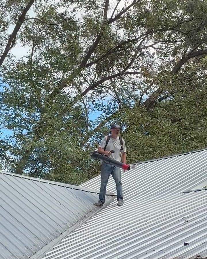Clear Flow technician on a metal roof with a backpack blower, clearing debris toward the eave above the porch